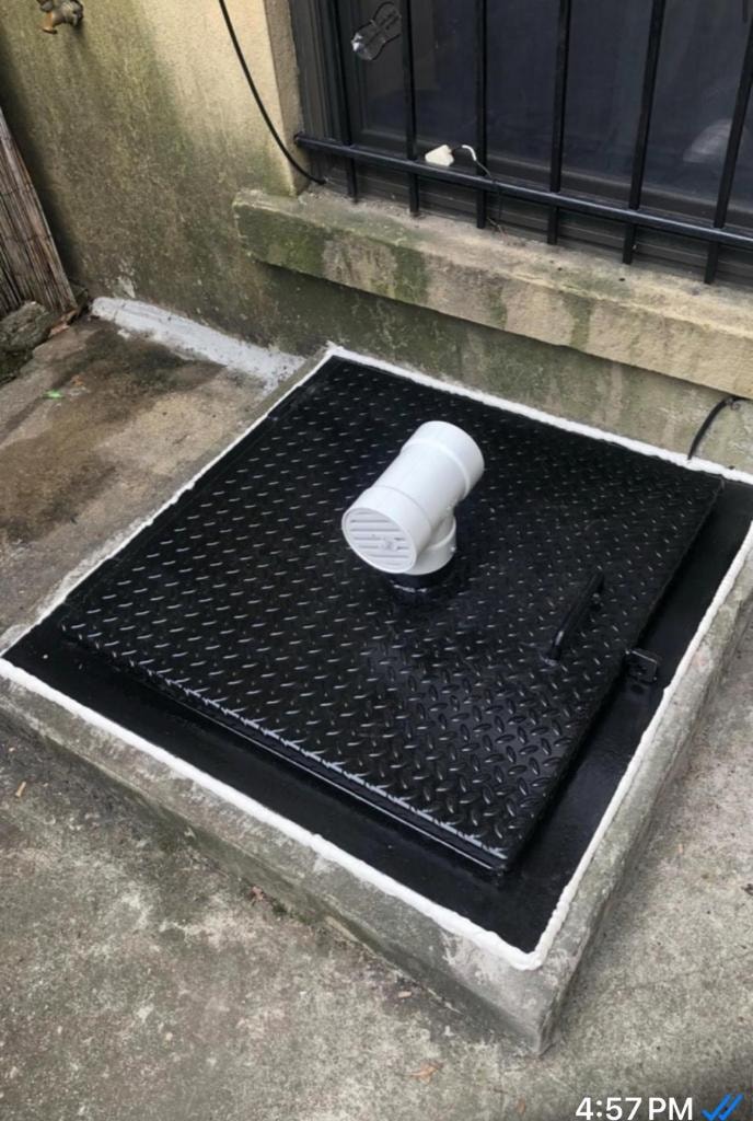 Black diamond-plate sidewalk hatch with white pipe vent