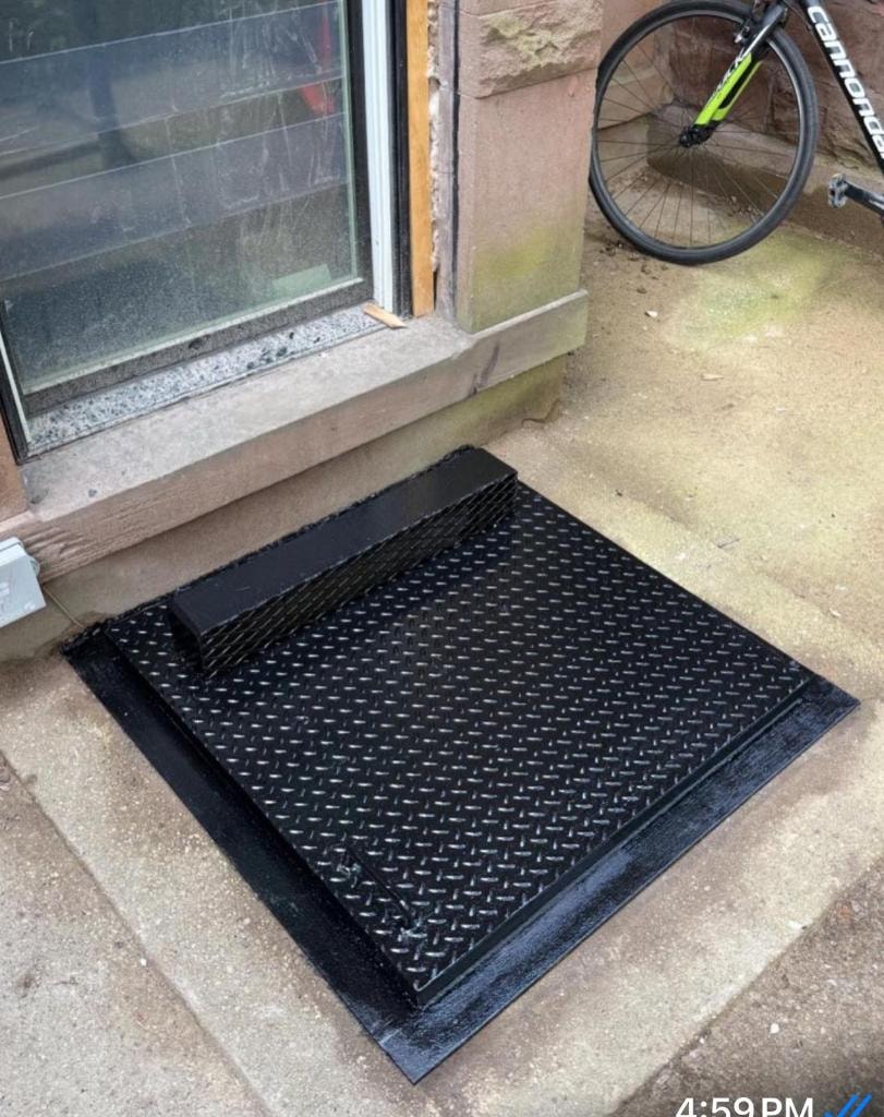 Black diamond-plate sidewalk hatch near bicycle