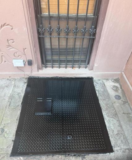 Black diamond-plate cellar hatch at ornate building entrance