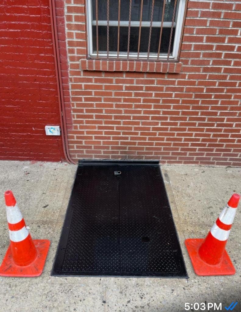 Black diamond-plate sidewalk cellar door with traffic cones