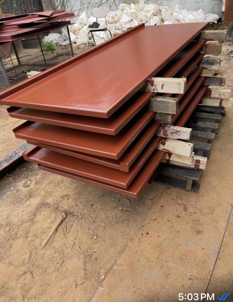 Stacked red primer metal door panels on pallets at fabrication yard