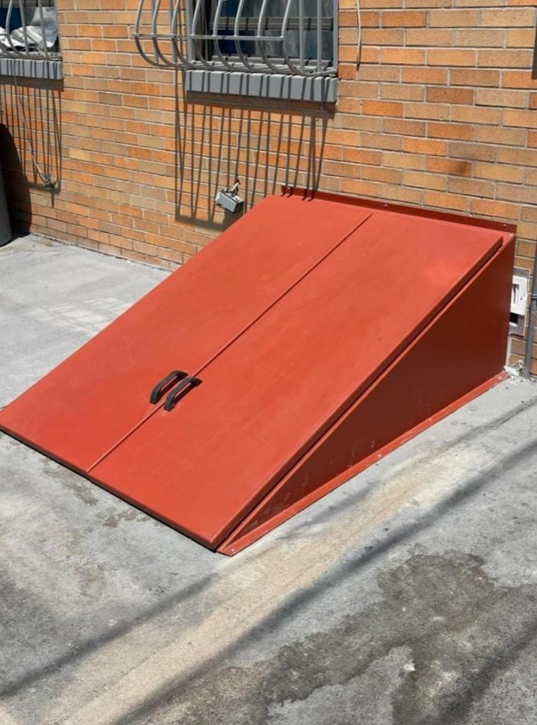 Red painted angled cellar door installed against brick building