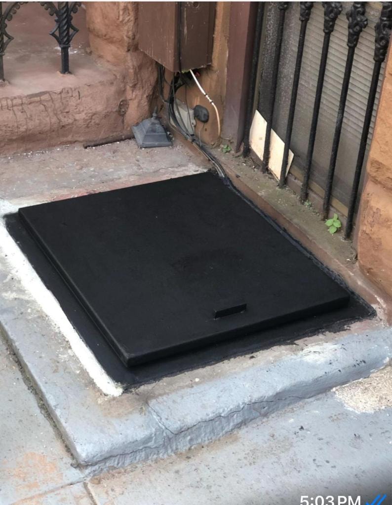 Flat black steel hatch installed flush at brownstone entrance